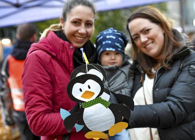 Zwei Frauen halten in ihrer Mitte ein kleines Kind auf dem Arm. Im Vordergrund ist eine selbstgebastelte Pinguin-Laterne zu sehen.