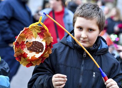 Ein Junge hält eine selbstgebastelte Laterne in der Hand. Die Laterne ist geschmückt mit einem Igel und Herbstblättern.
